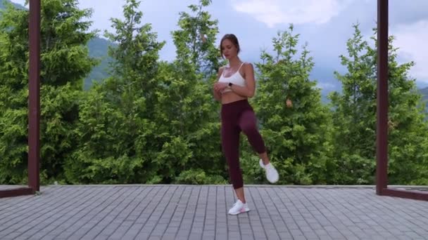 Jeune dame mince pratique le sport dans le parc, réchauffer les jambes avant l'entraînement — Video
