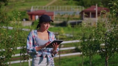 woman is monitoring growing of fruit trees in garden on eco farm