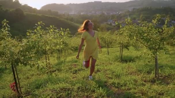Щаслива молода жінка проводить літні канікули в країні, бігає в саду під час заходу сонця — стокове відео