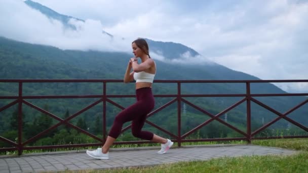 Young slender woman is doing physical exercises outdoors, squatting and training legs — Wideo stockowe