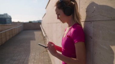 sportswoman is using mobile app with music for workout, standing in city street after training
