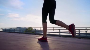 slender woman is jogging alone in early morning in city in summer day, closeup of female legs