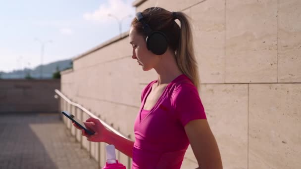 Sporty girl drinking water and enjoying music after training — Vídeo de Stock