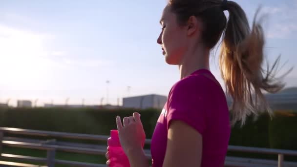 Zdrowa, aktywna kobieta biegnie wcześnie rano po mieście i pije wodę — Wideo stockowe