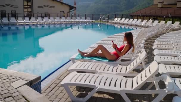 Отдыхающая девушка проверяет социальные сети перед купанием в бассейне — стоковое видео
