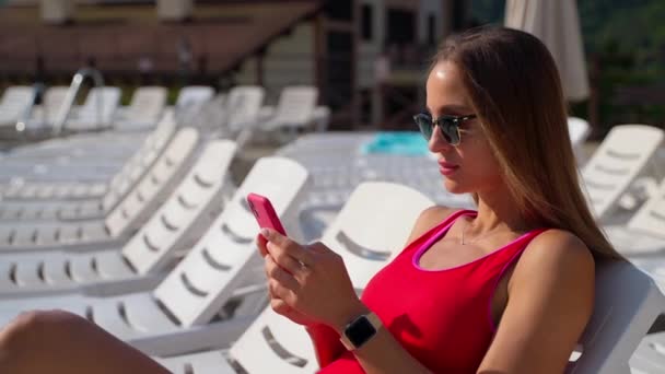 Giovane donna sexy sta visualizzando i social media nel moderno smartphone in hotel resort in estate — Video Stock