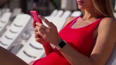 Yazın iskemlede rahatla güneşli yaz gününde bronzlaş, akıllı telefonlu seksi bayan.