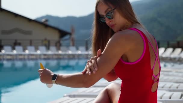 Verwendung von Sonnencreme im Kurhotel im Sommer, junge Frau ruht sich in der Nähe des Pools aus und bräunt sich — Stockvideo