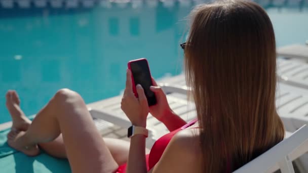 Mädchen in der Sonne am Pool und mit dem Handy — Stockvideo