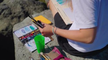 Sahilden akvaryuma deniz manzarası çizen kadın uçurumda oturuyor.