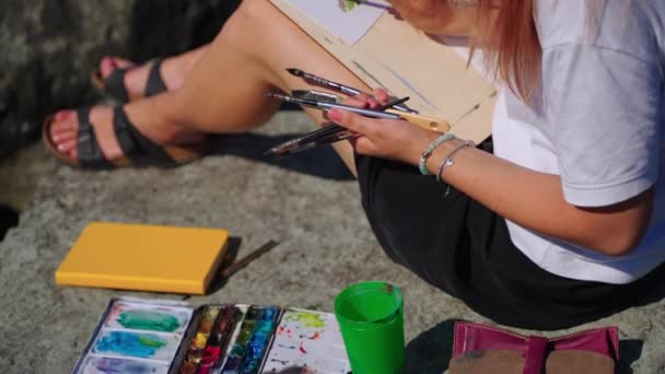 Schilderen uit de natuur aan zee kust in de zomer, jonge vrouw met aquarelverf — Stockvideo