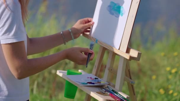 Художник малює пейзаж у пленері, використовуючи барвники, пензлик та мольберт — стокове відео