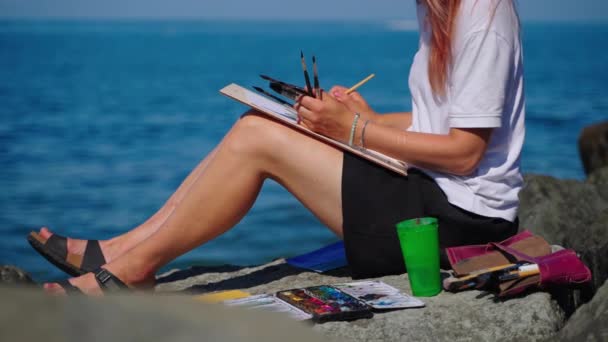 Talentosa artista mulher está pintando na praia, usando corantes aquarelle, trabalhando ao ar livre — Vídeo de Stock