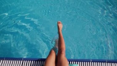 Tatilde olan bir kadın havuzda sallanan bacakları
