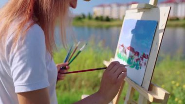 Kadın ressam gölün kıyısındaki parkta manzara çiziyor.