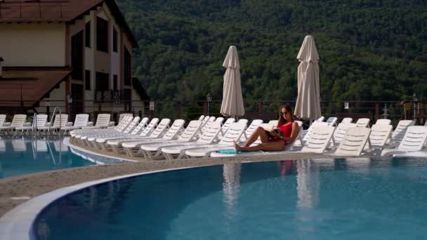 Γυναίκα αναπαύεται στο ξενοδοχείο θέρετρο στο βουνό το Σαββατοκύριακο, ξαπλωμένη σε lounge καρέκλα κοντά στην πισίνα — Αρχείο Βίντεο