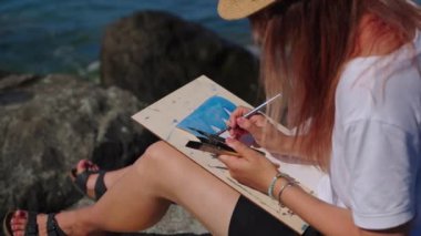 Genç kadın deniz manzarası çizmek için çalışıyor, plein havasında çalışıyor, akvaryumun resmini yapıyor.