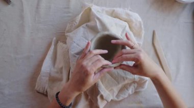 Stüdyoda çalışan bir kadın çömlekçinin yakın çekimi. Pikabın üstünde seramik kaseyi şekillendiren usta kadın, ellerle üstten görüş.