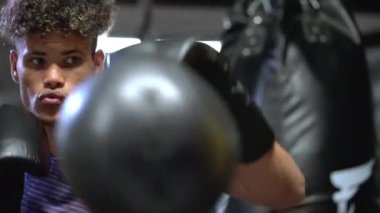 Genç siyahi adam Karayip boks kulübünde antrenman yapıyor, Afrikalı boksör kum torbası yumrukluyor, spor salonunda portre çekimi yapıyor.