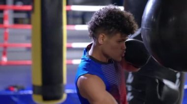 Genç Afrikalı sporcu boks antrenmanı yapıyor, antrenman salonunda kum torbasına vuruyor, profesyonel sporcu dövüşmeye hazırlanıyor.