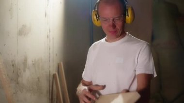 Marangoz atölyesinde koruyucu kulaklık, gözlük, işleme tahtası, orta yaşlı adam hobisi ve el yapımı ahşap işçiliği kullanarak çalışıyor.