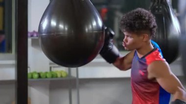 Profesyonel boks müsabakasına hazırlanan siyahi adam, antrenman salonunda kum torbasını asmaya çalışıyor.