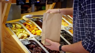 Erkek alışverişçi marketteki marketten kurutulmuş armutları alıyor. Kese kağıdına meyve koyuyor. Fiyat etiketlerine yazılan ürünler