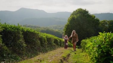 Tasasız küçük kız ve annesi yazın doğa yürüyüşünden zevk alıyorlar. Mutlu kadın ve kızı bahçede birlikte yürüyorlar.