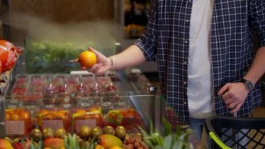 Markette sergilenen tropikal ve egzotik meyve çeşitleri arasından granadillayı seçen adam.