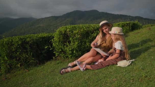 母亲带着女儿坐在草地上欣赏山水 妈妈教孩子画画 — 图库视频影像