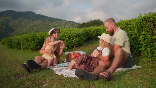 夏休みに幸せな家族のピクニック幸せな夫婦と子供たちは草の上に座って食事をしています — ストック動画