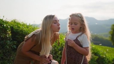 Sarışın bir anne ve kızının birlikte karahindiba üflediği yavaş çekim ve sonra sevgili anne çocuğa bir öpücük verir. Mutlu annelik, yeşil kırsaldaki aile