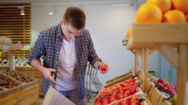 Vejetaryen marketten alışveriş yapıyor, sebze reyonundan organik domates seçiyor, insan çevre dostu süpermarketten kağıt torba kullanarak yiyecek alıyor.