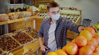 Erkek müşteri süpermarketten greyfurt alıyor, covid-19 'dan korunmak için yüz maskesi, pandemik dönemde alışveriş, tehlikeli omikron damgası, sağlıklı beslenme, vitamin zengini meyveler.