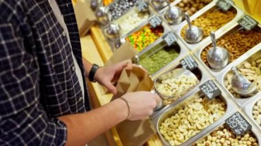 Süpermarkette alışveriş yapan erkek, ağırlıkla fındık alan, kağıt torbaya ceviz döken, markete servis yapan, fındık alan, fındık alan, yakın çekim gören, yiyecek isimlerinin yazılı olduğu Rus yazıtları olan erkek.