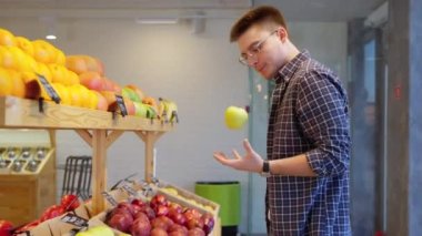 Genç adam meyve dükkanından alışveriş yapıyor, marketten elma seçiyor, süpermarketten erkek alışverişçi sağlıklı beslenme için organik meyve alıyor.