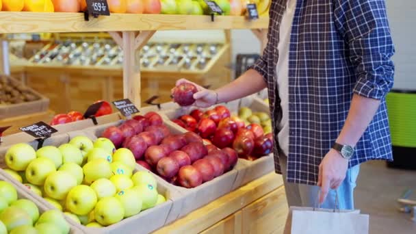 赤いりんごを取り 紙袋に入れる男のバイヤーの遅い動きのショット 屋台の果物のさまざまな種類は その名前は 価格のタグに書かれた 食料品店での買い物 — ストック動画
