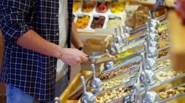 Tezgahtaki adam yavaş çekim yapıyor. Elinde tohumlar ve fındıklar var. O, küçük kağıt torbaya fındık döker. Manavda ya da süpermarkette alışveriş yapmak.