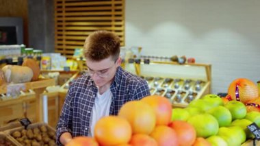 Genç adam marketten alışveriş yapıyor, turunçgilleri seçiyor, erkek alışverişçi sağlıklı ve organik yiyecekler alıyor, tatlı meyve, greyfurt ve portakal alıyor.