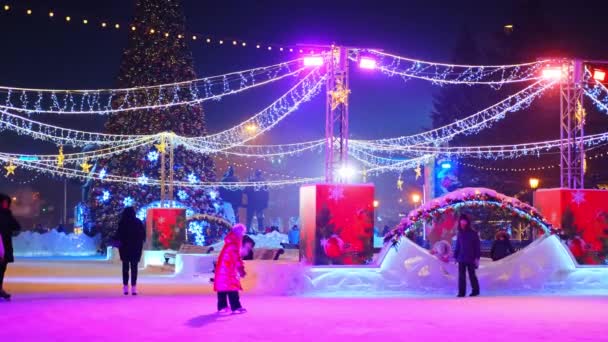 Nowosybirsk, Rosja, 31.12.2020: Ludzie jeżdżą na łyżwach wokół choinki z czerwoną gwiazdą. Nowy Rok dekoracji girlandy miasta — Wideo stockowe