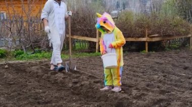 Tek boynuzlu at kostümlü çocuk, çiftçinin bahçeye patates ekmesine yardım ediyor.
