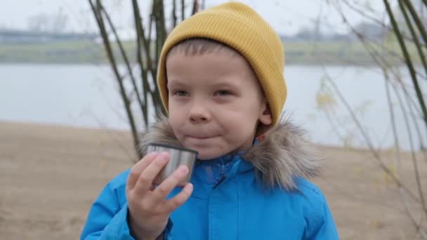 Chłopak pije herbatę w chłodny dzień na tle rzeki. — Wideo stockowe