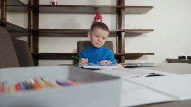 Beş yaşında bir çocuk kalemle resim çiziyor.