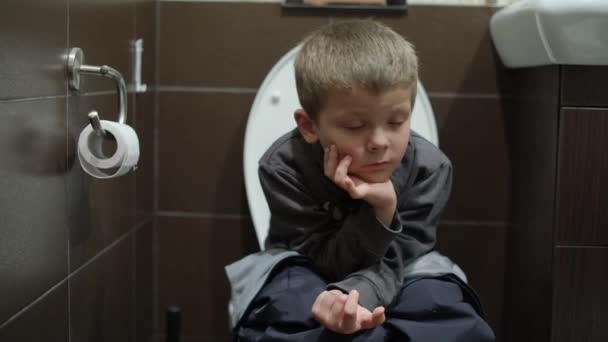 Een jongen zit op het toilet in het toilet — Stockvideo