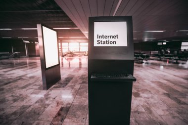 Boş bir reklam panosu şablonu olan bir havaalanının bekleme odasındaki bir internet terminalinin geniş açılı görüntüsü; halka açık internet erişimi olan modern bir bilgisayar standı ve bir afiş modeli
