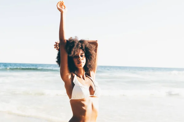 白いフリリービキニの中髪の若い黒人女性に焦点を当て 背景がぼやけている海の波があります 海の端に身を伸ばすアフリカ系アメリカ人女性 — ストック写真