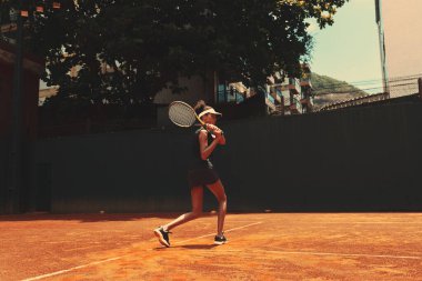Omzunun üzerinde tenis raketi tutan bir sporcu kadın, ayakları esnek ve dümdüz ileriye bakıyor. Dışarıda tek başına tenis oynayan Afrikalı bir kadın. Oyun sahasında egzersiz yapan bayan.