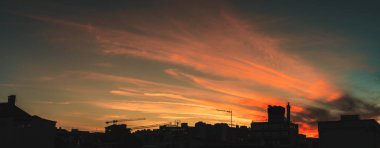 Akşam şehir manzarasının panoramik geniş açılı bir görüntüsü gökyüzü parlayan turuncu bir desen ve binaların üzerinde evler, çatılar, vinçler ve antenler, Lizbon, Portekiz
