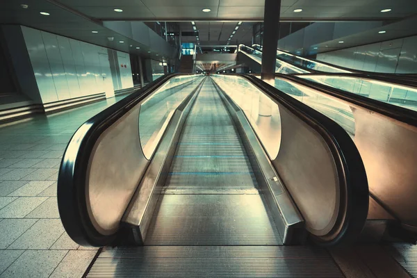 Front view of a chrome flat moving walkway in a subway or an office. Focus on an entrance on a travelator in an international airport or a mall; stairs, escalator, and neon lights in the background