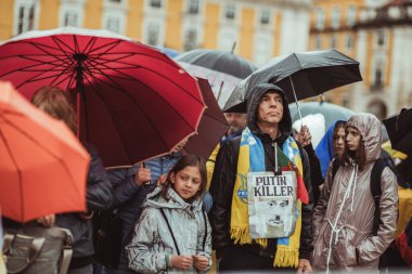 Lizbon, Portekiz - 20 Mart 2022: Rus işgali ve savaşa karşı Ukrayna 'yı desteklemek için bir protesto eylemi: Yağmurlu meydanda bir sıra protestan, Putin Katili posteri olan bir adam;